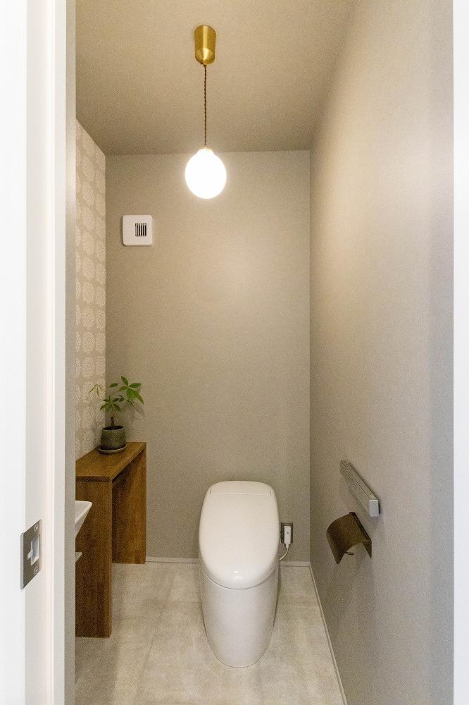 トイレの壁は一面だけ遊びを加えて。木製の造作棚がアクセント。